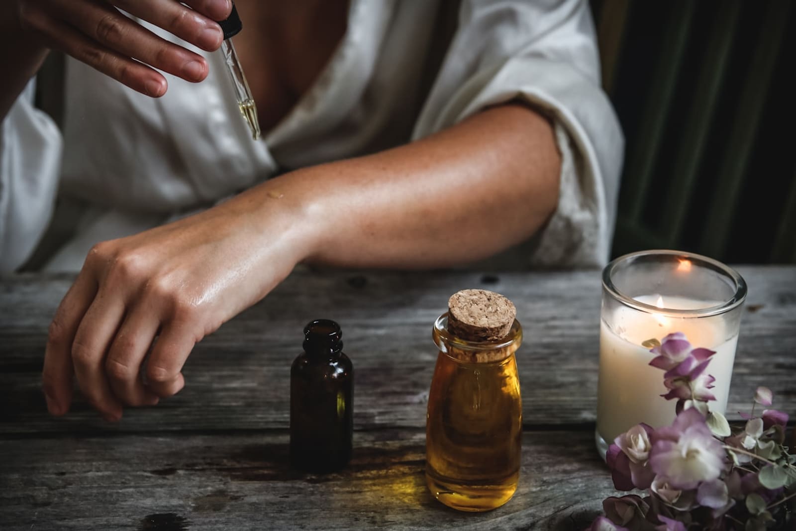 A warm, sunlit tabletop with amber and glass bottles, a lit candle, and soft flowers